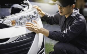 A person applies polishing compound to a fingertip near the headlight of a black car, preparing for Headlight Restoration New Orleans.
