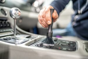A person uses a small brush to clean the control panel of a car's center console, showcasing the meticulous care offered by Car Detailing Services in Kenner.