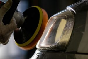 A person uses a polishing machine to buff the headlight area of a dark-colored vehicle, showcasing professional Headlight Restoration New Orleans services.