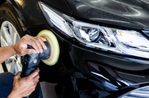 A technician from Mobile Car Detailing Hammond expertly uses a polishing machine to buff the front fender of a black car, focusing on the area near the headlight.