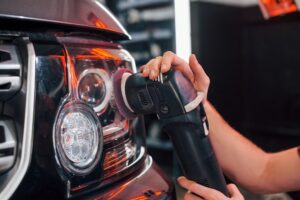 A person uses a polishing tool to buff the headlight of a car, wearing a glove for protection—demonstrating expert Headlight Restoration New Orleans services.
