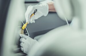A professional from Mobile Car Detailing Hammond, wearing white gloves, uses a small brush to meticulously clean the air vent inside a car.