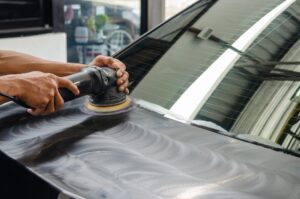 A person uses a polishing machine on the rear windshield of a car, creating visible swirl marks—an example of what Auto Paint Correction in New Orleans can help prevent and restore.