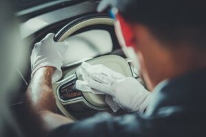 A person wearing white gloves wipes down a car steering wheel with a cloth, showcasing expert Auto Detailing in Slidell while cleaning the interior of the vehicle.