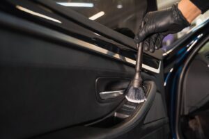 A gloved hand cleans the interior door panel of a car with a detailing brush, focusing on the area near the window controls—showcasing professional auto detailing in Slidell.