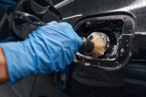 A person wearing blue gloves uses a brush to clean the area around a car’s fuel cap, providing thorough Mobile Auto Detailing in Mandeville, LA.