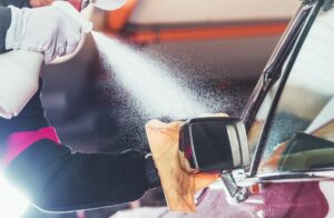 A person sprays cleaning solution onto a car's side mirror while wiping it with a yellow cloth, showcasing the precision of Mobile Auto Detailing in Mandeville, LA.