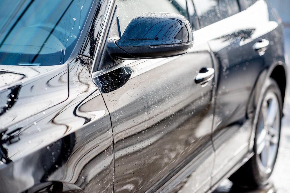 Close-up of a wet black car's side, showing the side mirror, front door, and water droplets—perfectly exemplifying the shine achieved with Mobile Auto Detailing in Metairie, LA.