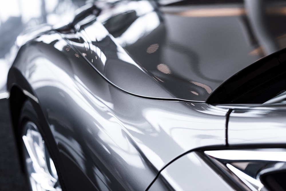 Close-up view of a shiny silver car’s hood and fender, enhanced by Ceramic Coating New Orleans, showing smooth lines and striking reflections of lights and surroundings on the surface.