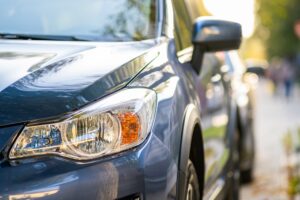 Close-up of the front left headlight and side of a parked dark blue car on a city street in LA, with a blurred background—ideal for showcasing professional Mobile Auto Detailing in Metairie.