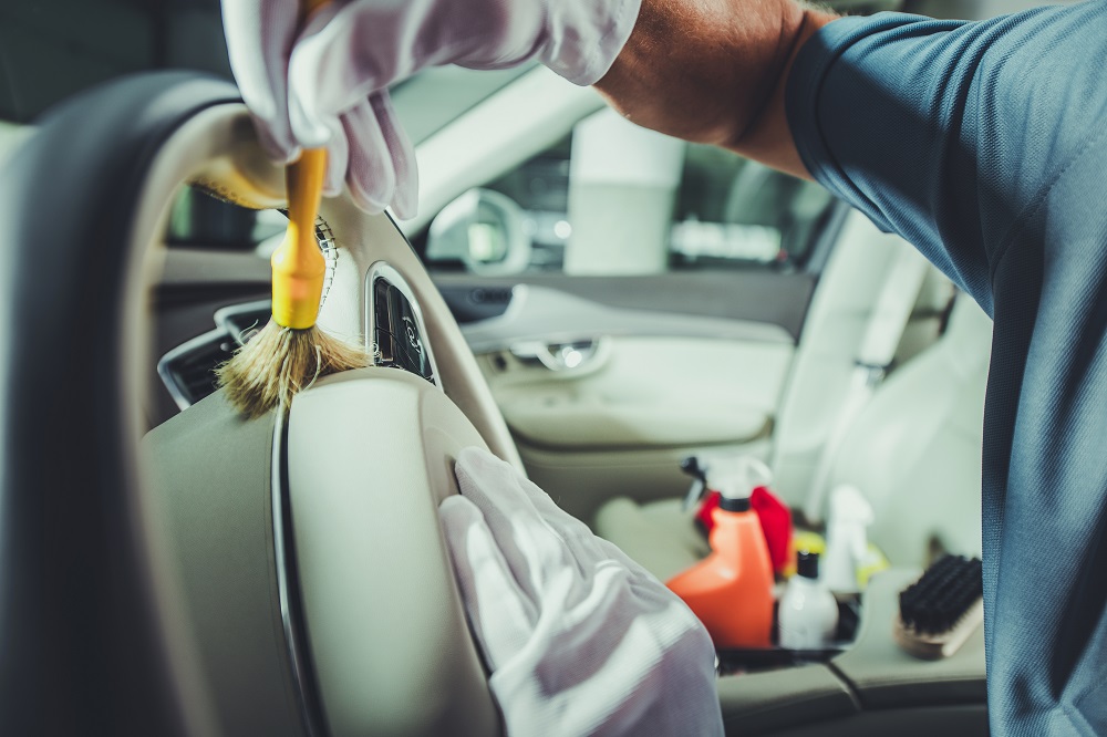 A person wearing gloves cleans a car’s interior, using a brush on the steering wheel. Cleaning supplies and spray bottles are visible in the background, showcasing Mobile Interior Car Detailing Services in New Orleans.