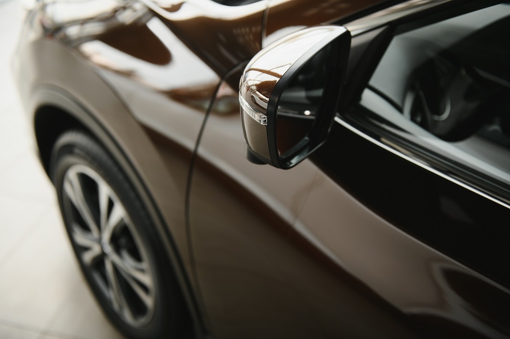 Close-up of a car's side mirror and front wheel, reflecting the surrounding indoor environment on the vehicle's glossy brown surface—an example of the shine achieved with Ceramic Coating New Orleans.
