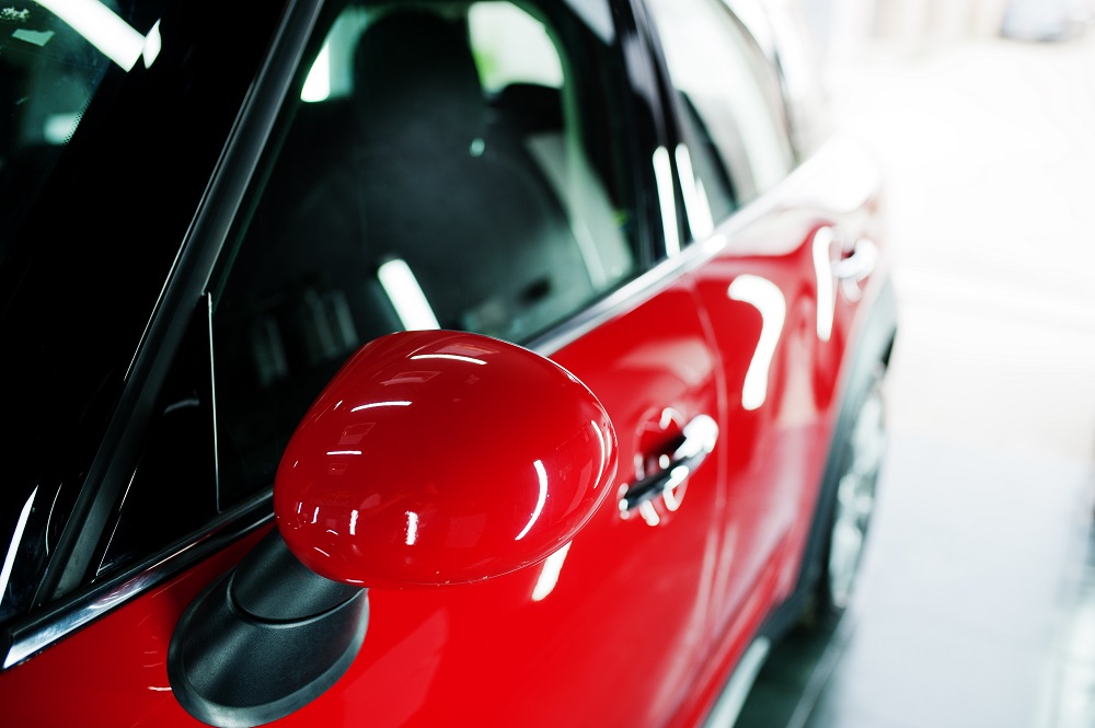Close-up view of the side of a red car, focusing on the red side mirror, window, and part of the front door in a brightly lit indoor setting—perfectly showcasing results from Mobile Auto Detailing in Metairie, LA.