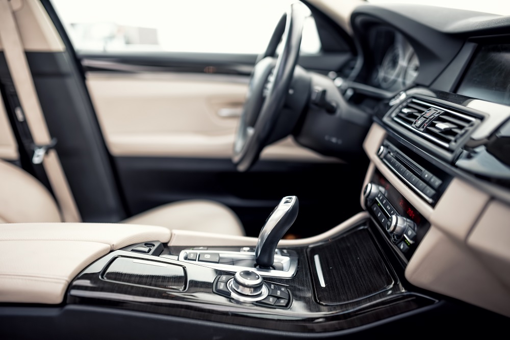 Close-up of a modern car's interior showing the gear shift, center console, dashboard controls, and beige leather seats—perfect results from Mobile Interior Car Detailing Services in New Orleans.