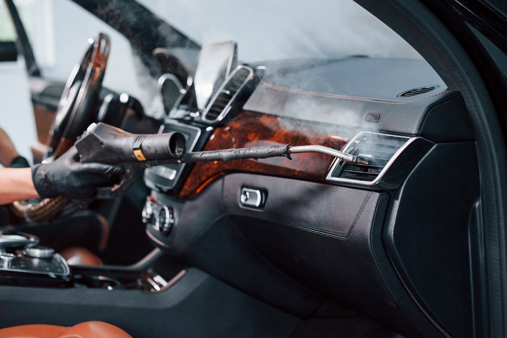 A person uses a steam cleaner to clean the air vent on the dashboard, showcasing Mobile Interior Car Detailing Services in New Orleans.