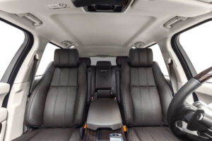 Interior view of a modern car featuring black leather front and rear seats, a central armrest, and part of the steering wheel, highlighting premium interior detailing.
