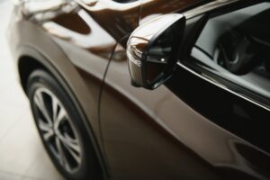 Close-up view of a car's side mirror and front wheel, with reflections gleaming on the shiny brown exterior—showcasing the quality of Car Detailing New Orleans.