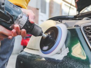 A person uses a power drill with a polishing pad to clean the headlight of a green car, demonstrating expert Car Detailing New Orleans techniques.