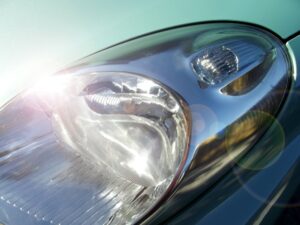  Close-up of a car’s headlight after Headlight Restoration New Orleans, with sunlight reflecting off the shiny surface and creating lens flares in the image.