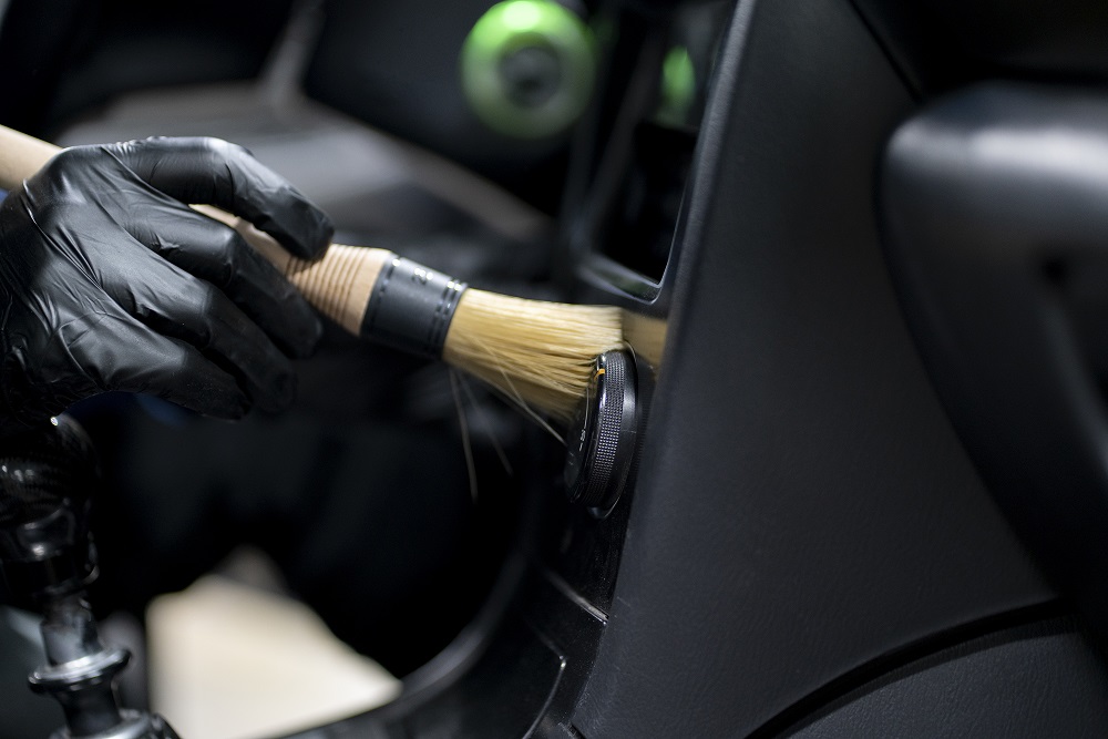 A person wearing black gloves cleans a car's interior vent with a bristle brush, showcasing expert Auto Detailing Abita Springs services.