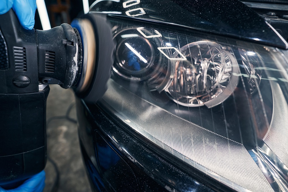 A person uses a polishing tool to clean and restore the headlight of a black car during an Auto Detailing Abita Springs service.