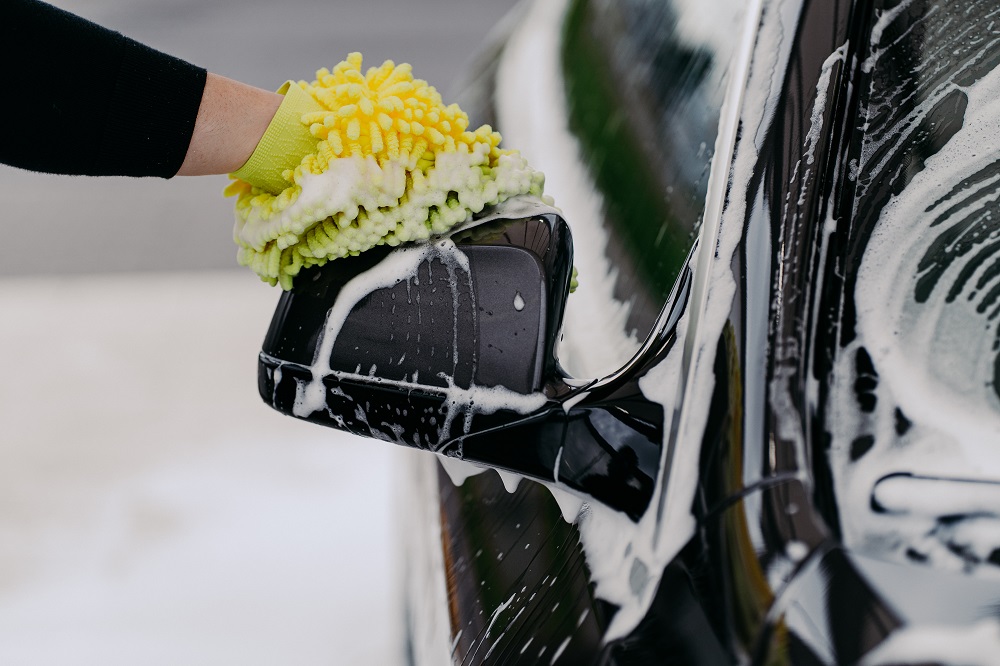 A person wearing a yellow glove uses a soapy sponge to clean the side mirror of a black car, showcasing professional auto detailing Abita Springs services.