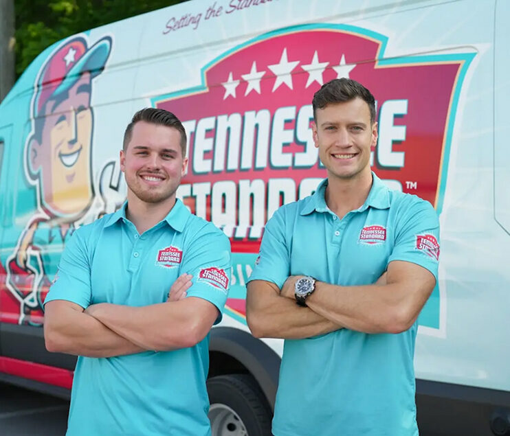 Bobby and Kelton wearing light blue polo shirts stand with arms crossed in front of a Tennessee Standard-branded van.