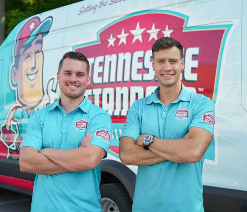 Boby and Kelton wearing light blue polo shirts stand with arms crossed in front of a Tennessee Standard-branded van.